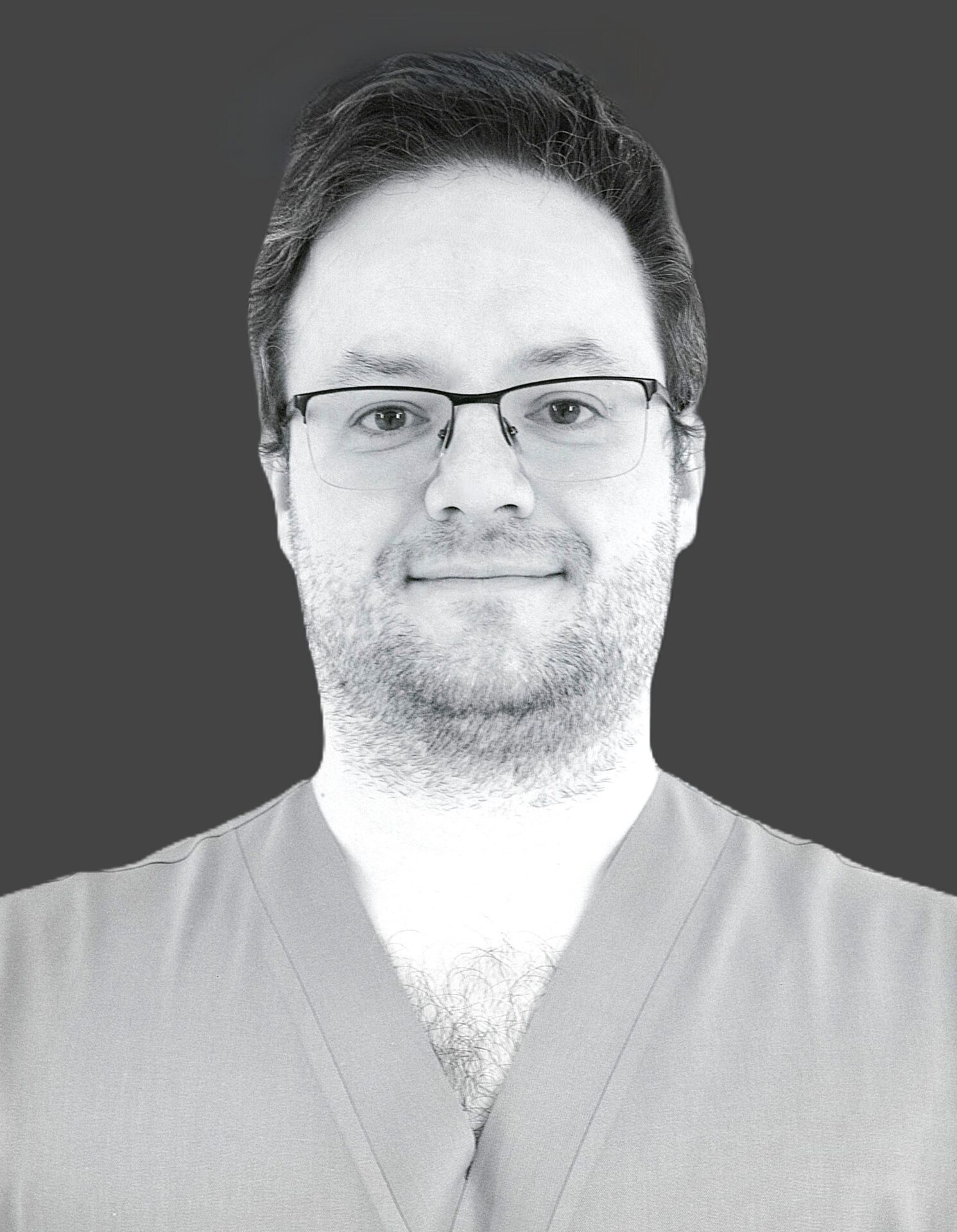 Vīrietis ar brillēm un pelēku medicīnas apģērbu, pozē uz tumša fona. Rīgas 1. slimnīcas darbinieks.