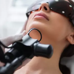 Sieviete ar aizsargbrillēm, saņemot ādas ārstēšanu Rīgas 1. slimnīcā. Redzams medicīniskais instruments.