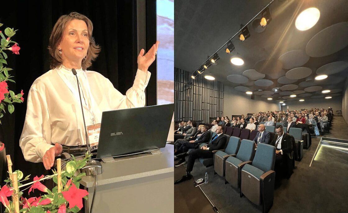 Konference Rīgas 1. slimnīcā, runātāja pie datora, auditorija ar klausītājiem.