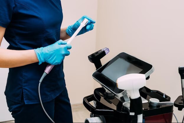 Mediķis ar zilu cimdu tur medicīnas ierīci blakus ekrānam Rīgas 1. slimnīcā.