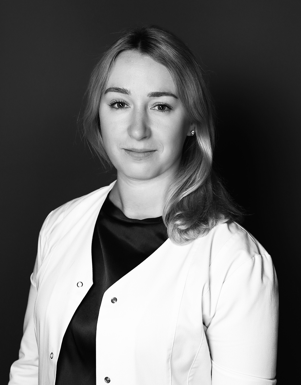 Sieviete ar blondiem matiem, baltā apģērbā, skatās uz kameru. Rīgas 1. slimnīcas darbiniece.