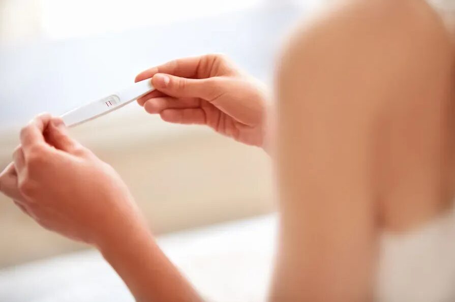 Sieviete tur grūtniecības testu ar divām svītrām, norādot uz pozitīvu rezultātu.
