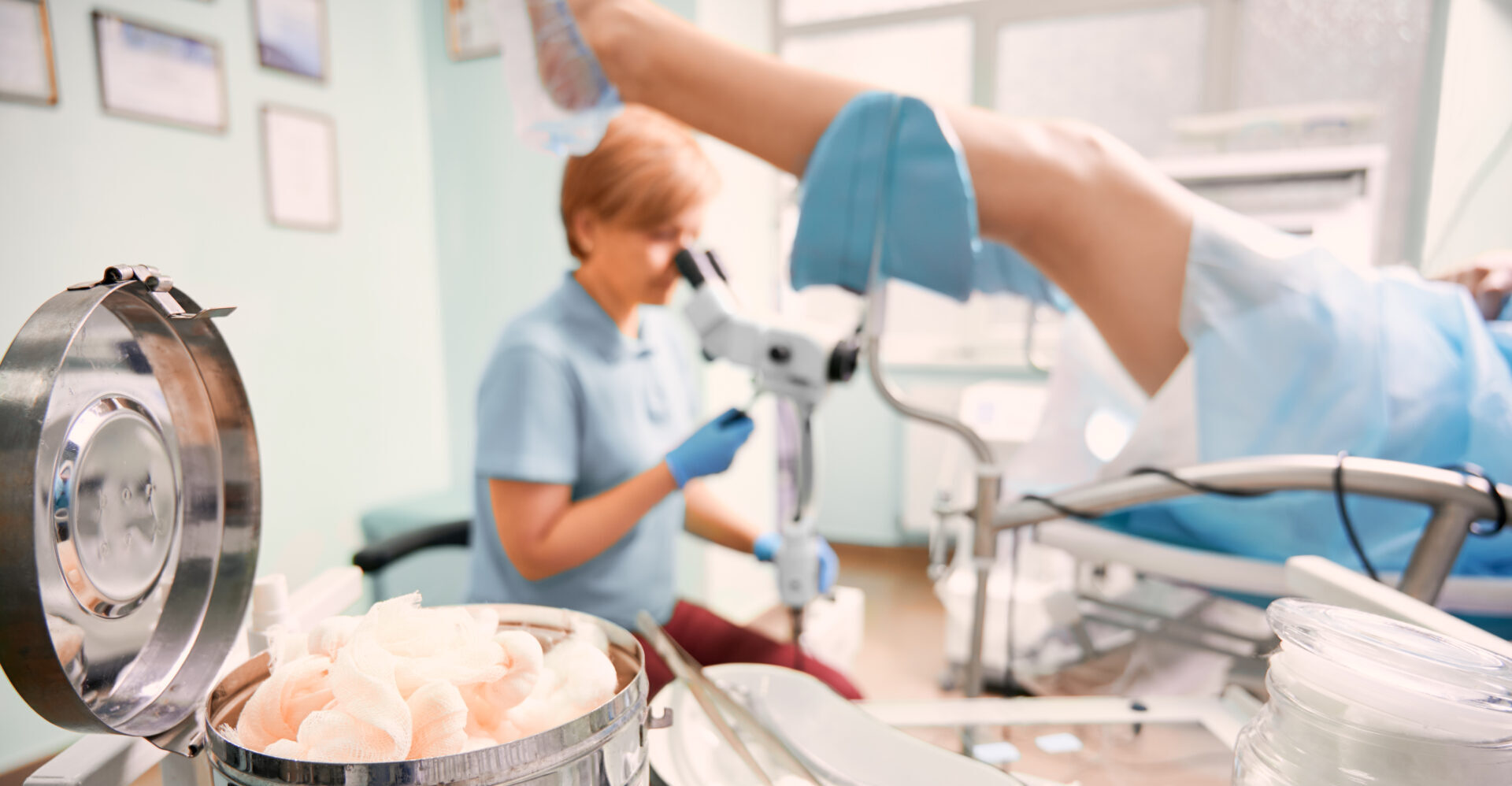 Medicīnas procedūra Rīgas 1. slimnīcā, redzama pacienta kāja un ārsta darbs ar mikroskopu.