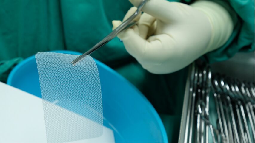 Ķirurgs ar cimdiem tur medicīnisku materiālu, kas atrodas zilo traukā. Fons ar instrumentiem.