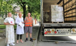 Trīs cilvēki stāv pie kravas automašīnas, kas piegādā preces Rīgas 1. slimnīcai. Redzami sarkans krusts un dokumenti.