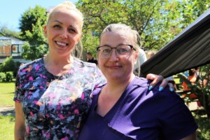 Divas sievietes, medicīnas darbinieces, pozē saulainā dārzā pie Rīgas 1. slimnīcas.