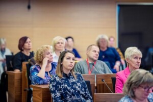 Attēlā redzama auditorija ar cilvēkiem, kas klausās prezentācijā Rīgas 1. slimnīcā.