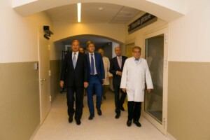 Vīrieši, tostarp ārsti, staigā pa Rīgas 1. slimnīcas koridoru pie durvīm uz "Personāla ģērbtuvi".