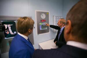 Divi vīrieši apspriež medicīniskos attēlus pie monitora Rīgas 1. slimnīcā. Redzams pulkstenis un skaitītājs.