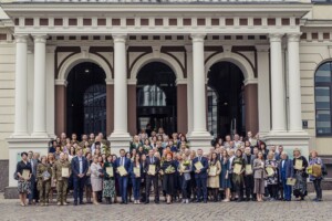 Rīgas 1. slimnīcas darbinieki grupā ar diplomiem pie ēkas ieejas. Daži tur ziedus.
