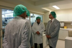 Četri cilvēki medicīniskās drēbēs un cepurēs Rīgas 1. slimnīcas telpās. Redzama medicīnas iekārta fonā.