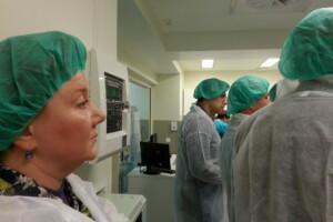 Grupas cilvēku ar zaļām cepurēm un baltām apģērbu daļām, Rīgas 1. slimnīcas telpā.