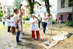 Grupas cilvēku apmācība ar loku un bultām Rīgas 1. slimnīcas pagalmā. Redzami dažādi apģērbi un rīki.