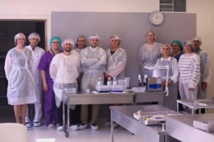Rīgas 1. slimnīcas darbinieki stāv grupā, tērpušies aizsargapģērbā, laboratorijas vidē.