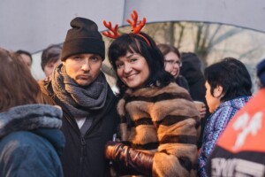 Divi cilvēki, vīrietis un sieviete, pozē kopā, apģērbtā ziemas apģērbā un svētku aksesuāros.
