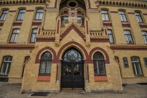 Rīgas 1. slimnīcas ēkas fasāde ar izteiksmīgu arhitektūru un melnām durvīm centrā.