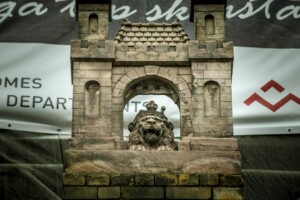 Mākslas darbs ar lauvas figūru un celtni, fons ar tekstu "Rīgas 1. slimnīca".