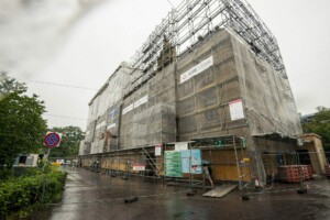 Rīgas 1. slimnīcas būvniecība, pārklāta ar plēvi un skavām, lietus laikā. Redzama ceļa zīme "Aizliegts stāvēt".