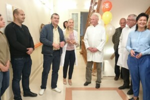 Rīgas 1. slimnīcas darbinieki un viesi svin pasākumu, fons ar baloniem un numuru 8.