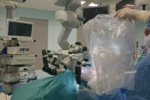 Ārsts sagatavo robotu operācijai, valkājot medicīniskās cimdus un masku, operāciju telpā.