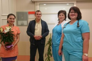 Četri cilvēki Rīgas 1. slimnīcā, viens ar ziediem, divi medicīnas darbinieki un viens vīrietis.