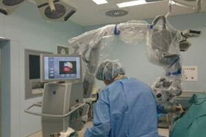 Operāciju telpa ar robotu un monitoru. Ārsts veic procedūru, tērpies medicīniskajā apģērbā.