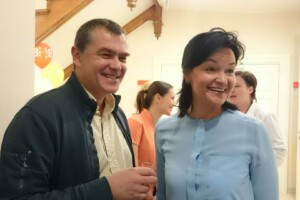 Divi cilvēki smaida un sarunājas Rīgas 1. slimnīcā, fona dekorācijas ar baloniem.
