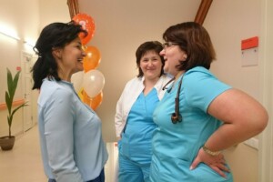 Trīs medicīnas darbinieces sarunājas Rīgas 1. slimnīcā, fona dekorācijas ar baloniem.