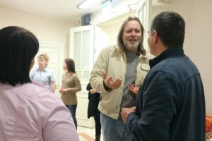 Cilvēki sarunājas telpā, Rīgas 1. slimnīcas apmeklētāji un darbinieki. Redzamas vairākas personas.