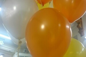 Baloni dažādās krāsās, tostarp oranžā un baltā, grupā ar cilvēkiem Rīgas 1. slimnīcā.