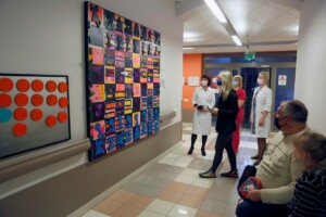 Divi mākslas darbi pie sienas, cilvēki apspriež tos Rīgas 1. slimnīcā. Redzami arī medicīnas darbinieki.