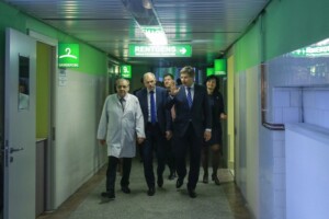 RD_komis_slimn_20160129 Grupa cilvēku, tostarp ārsts, staigā pa Rīgas 1. slimnīcas koridoru, virzieni uz "Garderope" un "Rentgens".