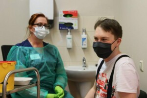 Pacients un medicīnas darbinieks ar maskām, medicīniskā aprīkojuma fons, Rīgas 1. slimnīca.