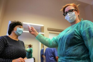 Mediķis mēra temperatūru pacientam Rīgas 1. slimnīcā, abas personas valkā sejas maskas.