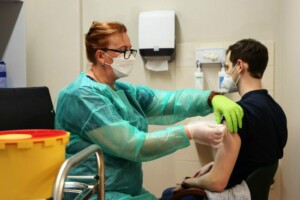 Mediķis vakcinē pacientu, valkājot masku un aizsargapģērbu, Rīgas 1. slimnīcā. Redzams arī atkritumu konteiners.