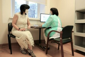 Divas sievietes, viena medicīnas darbiniece, otra pacientka, sarunā pie datora Rīgas 1. slimnīcā.