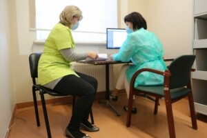 Divas medicīnas darbinieces strādā pie galda, izmantojot datoru un dokumentus Rīgas 1. slimnīcā.