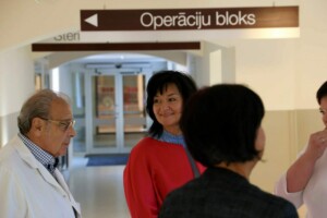 Attēlā redzami cilvēki Rīgas 1. slimnīcas operāciju blokā, virziena zīme "Operāciju bloks" fonā.