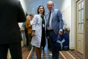 edf Divi cilvēki, ārsts baltā mētelī un vīrietis uzvalkā, stāv Rīgas 1. slimnīcas gaiteņos.