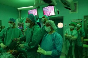 cof Ārsti un medicīnas personāls operāciju zālē, zaļās drēbēs, ar medicīnas aprīkojumu un ekrāniem.