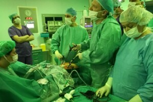 cof Operācijas telpa ar medicīnas personālu, kas veic procedūru. Redzami instrumenti un pacients uz operāciju galda.