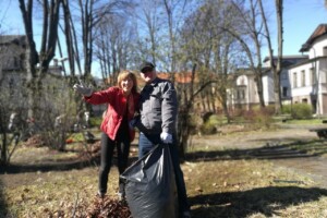 edf Divi cilvēki dārzā, viens ar melnu maisu, otrs sveicina. Rīgas 1. slimnīcas apkārtnes sakopšana.