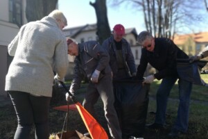 edf Cilvēki strādā dārzā, vācot atkritumus melnās maisos un izmantojot grābekļus. Rīgas 1. slimnīcas apkārtne.