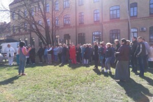 dav Grupas cilvēku sanāksme Rīgas 1. slimnīcas pagalmā, saulaina diena, runātājs priekšā.