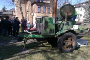 dav Zaļš traktors ar katlu, ap to pulcējušies cilvēki, Rīgas 1. slimnīcas pagalmā saulainā dienā.