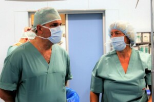 Divi mediķi operāciju telpā, ģērbušies zaļās drēbēs un maskās, gatavojas procedūrai. Rīgas 1. slimnīca.
