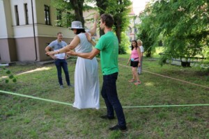 Cilvēki Rīgas 1. slimnīcas pagalmā piedalās aktivitātē uz virves, viens cilvēks balansē, citi atbalsta.