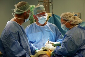 Trīs ķirurgi operācijas laikā, valkājot medicīniskos tērpus un aizsargbrilles. Rīgas 1. slimnīca.