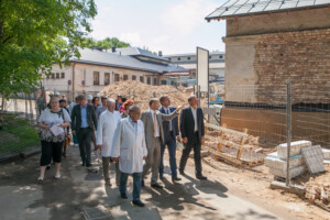 Grupa cilvēku, tostarp mediķi, apskata būvniecības darbus Rīgas 1. slimnīcas teritorijā.