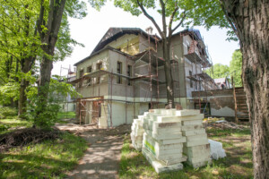 Rīgas 1. slimnīcas ēka ar renovācijas darbiem, redzami skaldīti kokmateriāli un būvniecības skala.